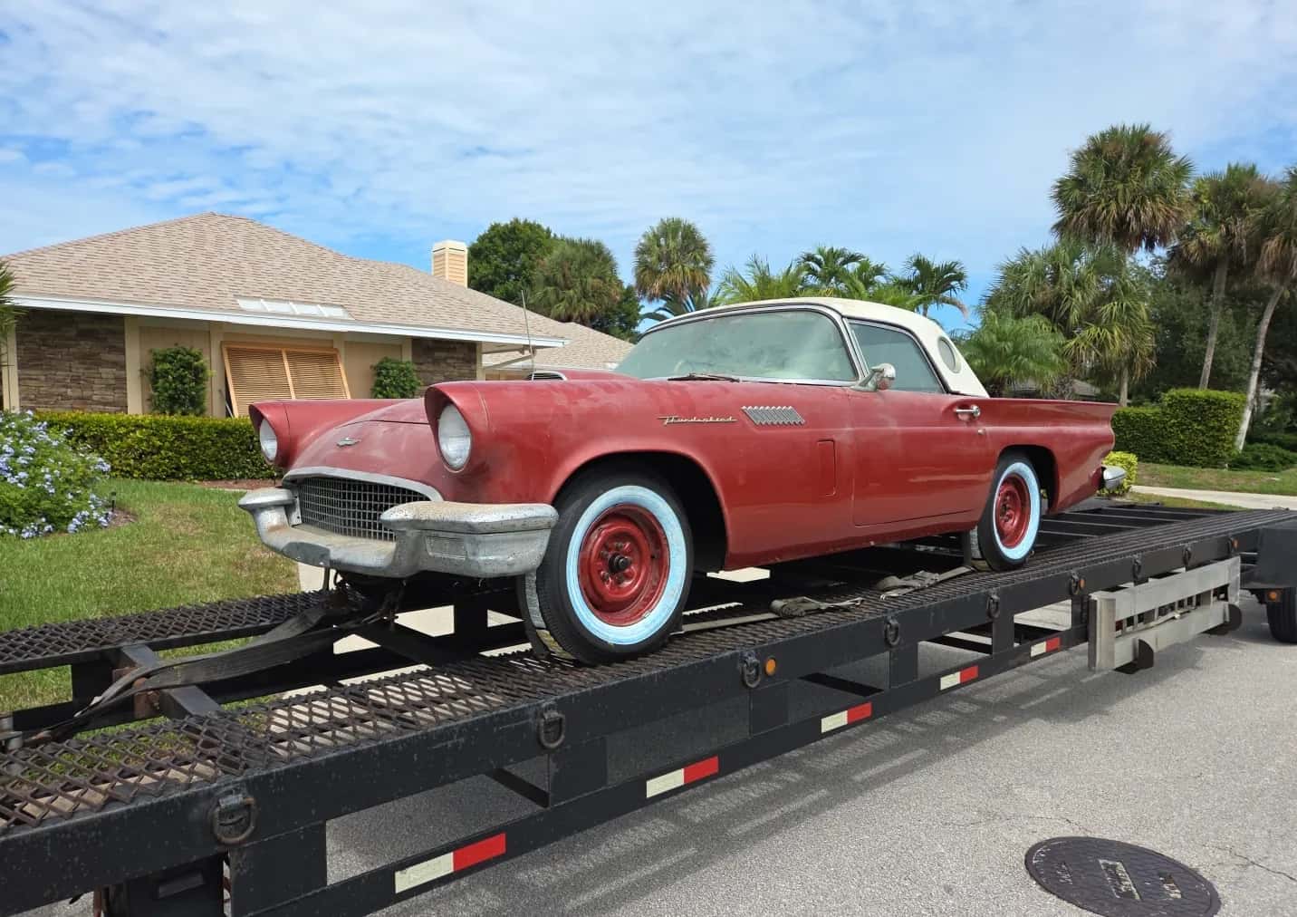1957 Ford Thunderbird strapped to a carrier's trailer on a residential street